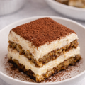 Tiramisu dessert with caramel sauce being poured over a piece of cake on a white plate.